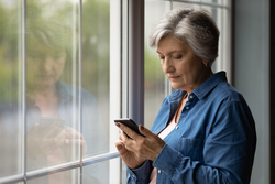 Important message. Serious aged latin female pensioner stand by picture window at home hold cell text in messenger app. Focused older woman thinking on email received from bank write answer. Copyspace