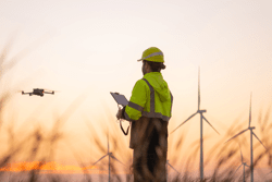 Engineers male flying drone surveying and checking wind turbines from the high angle view of the field during beautiful sunset. using drone technology for work.; Shutterstock ID 2602929959; purchase_order: -; job: -; client: -; other: -